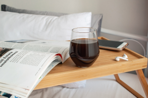 A book, a glass of wine and an iPhone on a bedside table with pillows in the background.